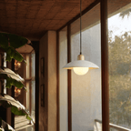 Clérachic white pendant light glowing beside glazed doors overlooking a lush green courtyard with banana leaves.