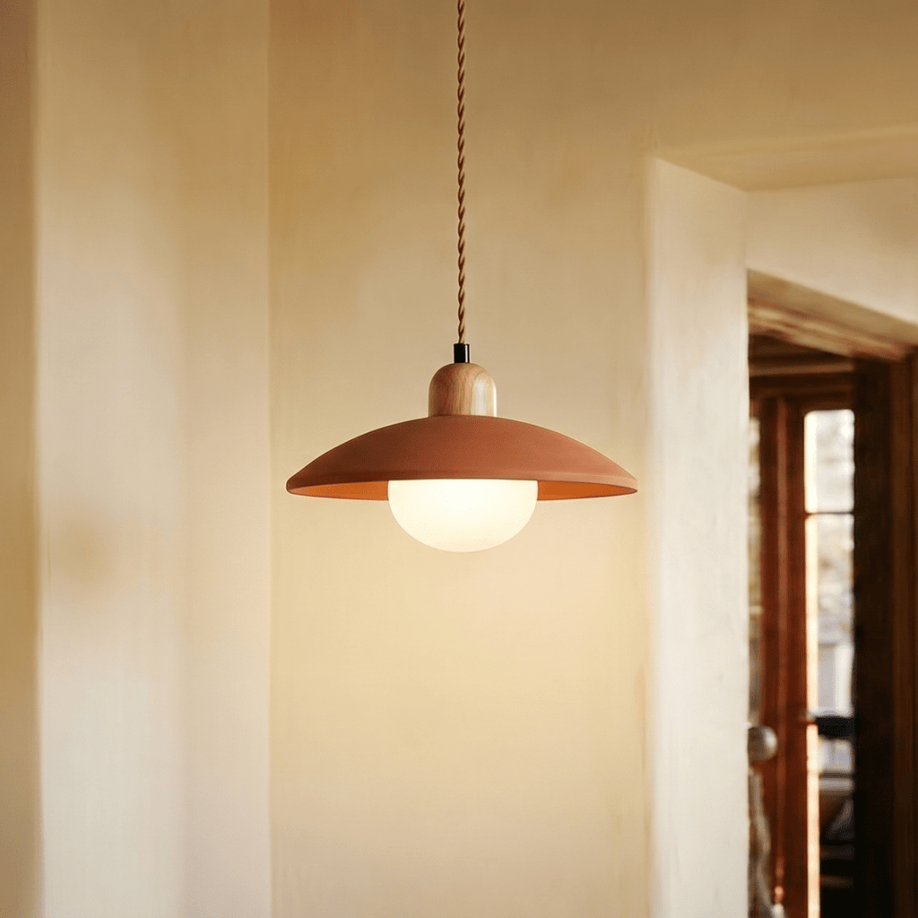 Clérachic orange pendant light glowing in a plaster hallway beside a timber door leading to a sunlit room.