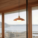 Clérachic orange pendant light glowing beside a window overlooking a calm bay beneath timber ceiling beams.
