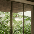 Clérachic white pendant light glowing beside floor-to-ceiling windows overlooking dense tropical greenery.