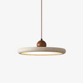 A Clérachic pendant with a flat, ring-edged travertine-look disc shade, lit from beneath, hung from a rust-brown cord with a walnut-toned bead, on white.