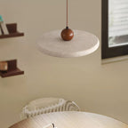 A cream stone-look disc and wooden bead of this Clérachic pendant seen from below, with shelves and a framed print behind.