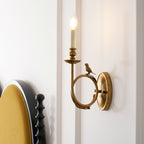 Clérachic's sconce mounted above a black tufted headboard with a mustard cushion, its candle bulb glowing warmly.