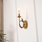 Clérachic's sconce glowing softly on the wall, with green plant fronds framing the lower corner of the shot.