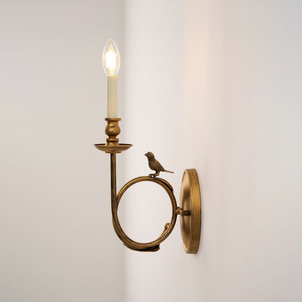 The Clérachic sconce shown at a tighter side angle, candle bulb lit and the bird resting where the ring meets the wall plate.