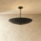 Clérachic perforated disc pendant light in matte black, hung from a plaster ceiling and photographed in studio.