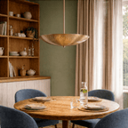 Clérachic brass perforated disc pendant light lit above a round table with blue chairs and a wooden hutch.