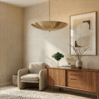 Clérachic brass perforated disc pendant light lit beside an armchair, a green lamp and a wooden sideboard.