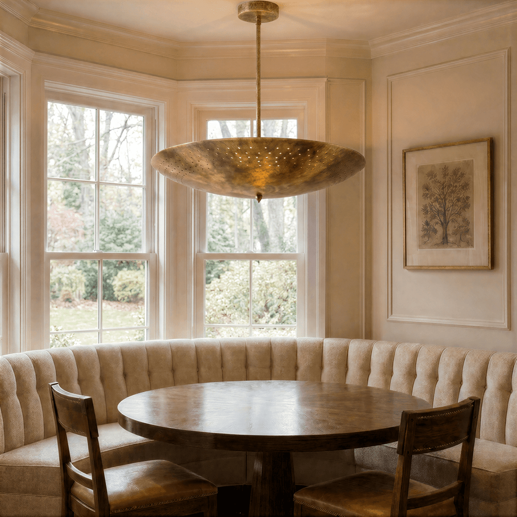 Clérachic vintage brass perforated disc pendant light lit above a round table in a curtained bay-window nook.