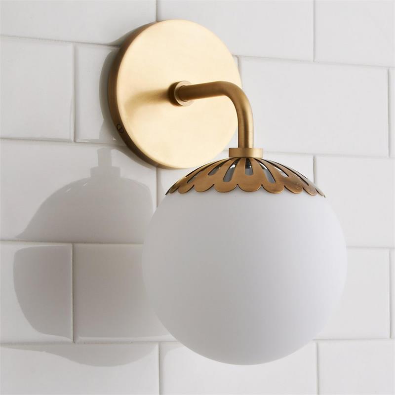 Clérachic Petal-Cap Opal Globe Wall Sconce in brass, single head, its scalloped cap set over the opal globe on white tile.