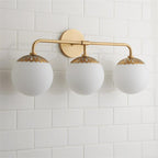 Three-head Clérachic Petal-Cap Opal Globe Wall Sconce in brass, three opal globes evenly spaced across white tile.
