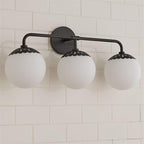 Clérachic Petal-Cap Opal Globe Wall Sconce in black, three heads spanning a white-tiled bathroom wall.
