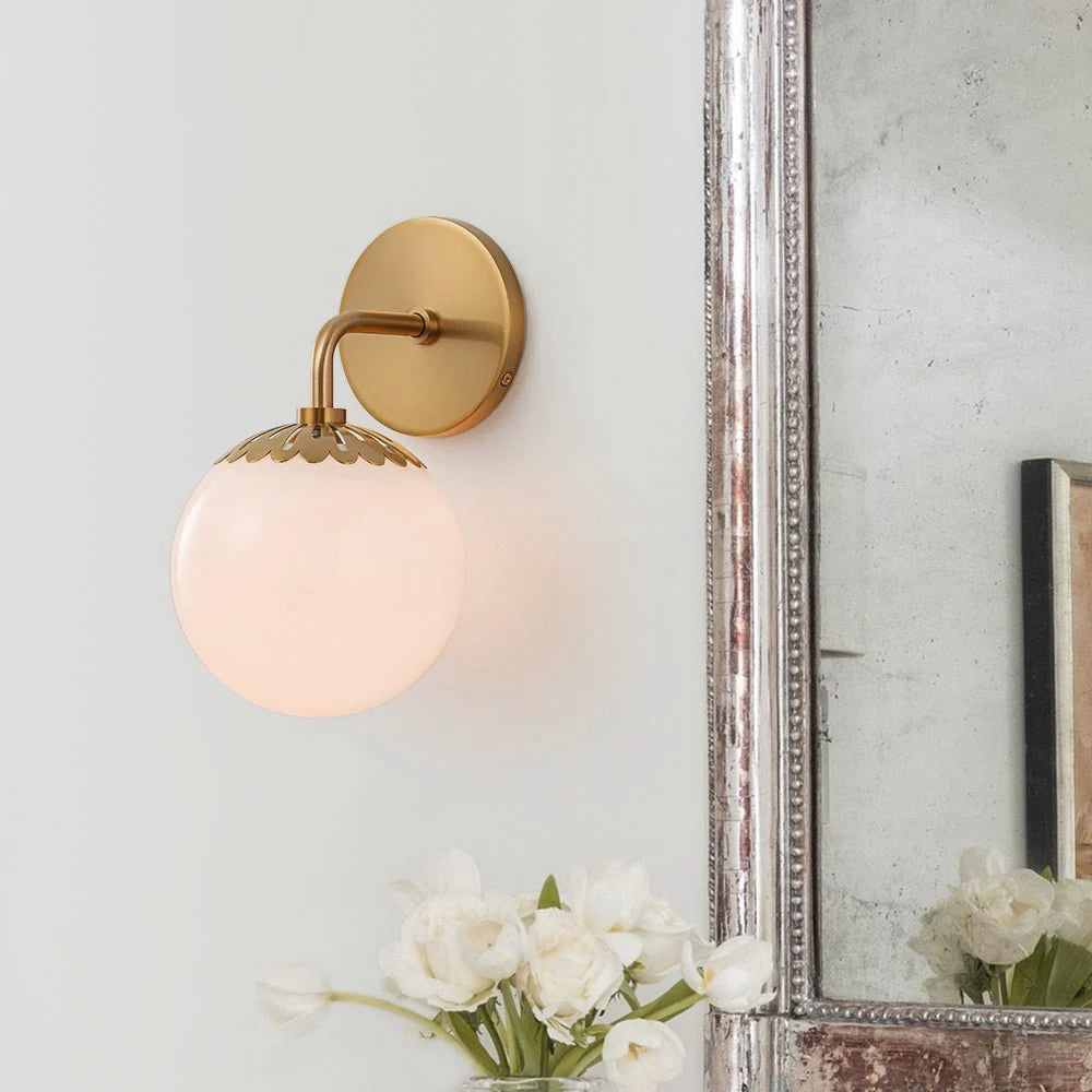Brass Clérachic Petal-Cap Opal Globe Wall Sconce glowing beside an antique silver mirror, white tulips below.