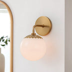 Single brass Clérachic Petal-Cap Opal Globe Wall Sconce lit next to an arched gold-framed mirror.