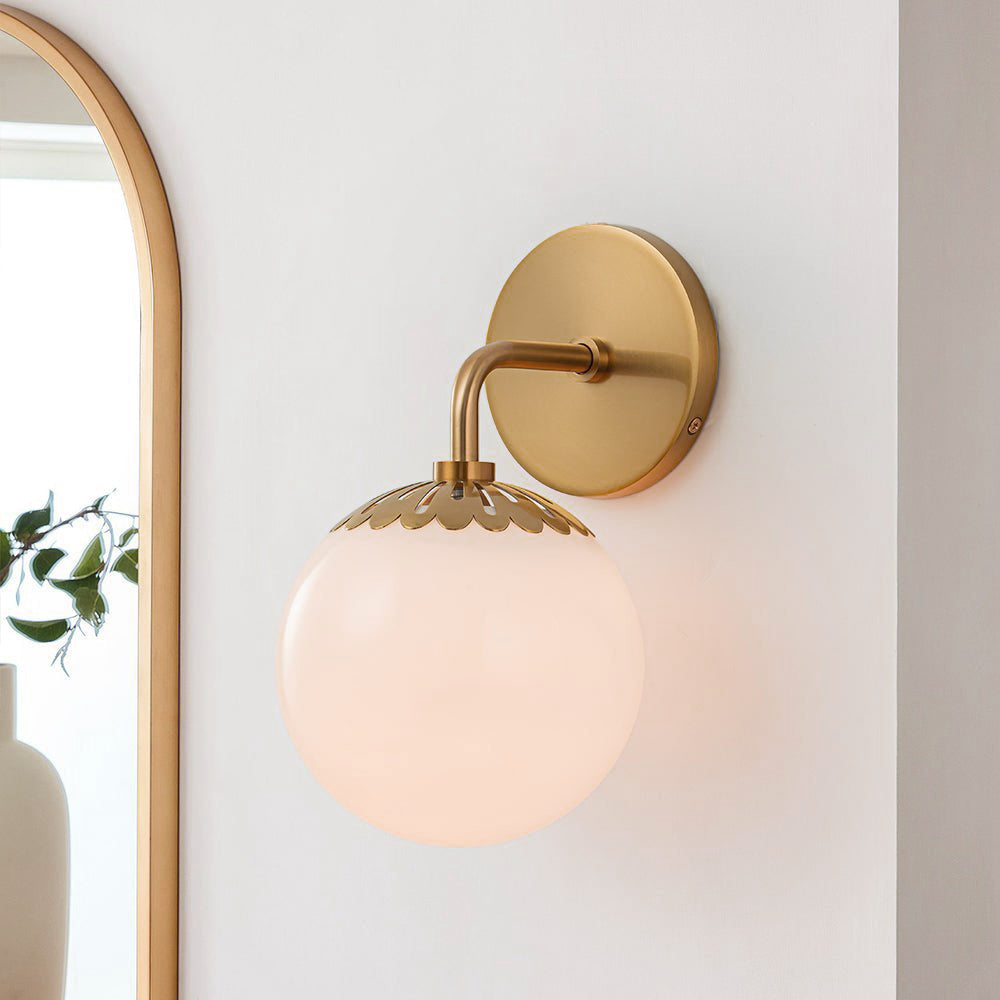 Single brass Clérachic Petal-Cap Opal Globe Wall Sconce lit next to an arched gold-framed mirror.