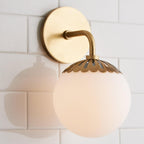 Angled close-up of the brass Clérachic Petal-Cap Opal Globe Wall Sconce, curved arm dropping to the scalloped cap.