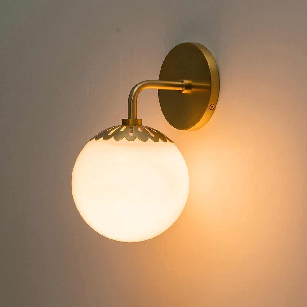 Brass Clérachic Petal-Cap Opal Globe Wall Sconce switched on, throwing a warm pool of light across a plain wall.