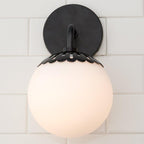 Head-on view of the black Clérachic Petal-Cap Opal Globe Wall Sconce, the arm hidden behind the opal globe.