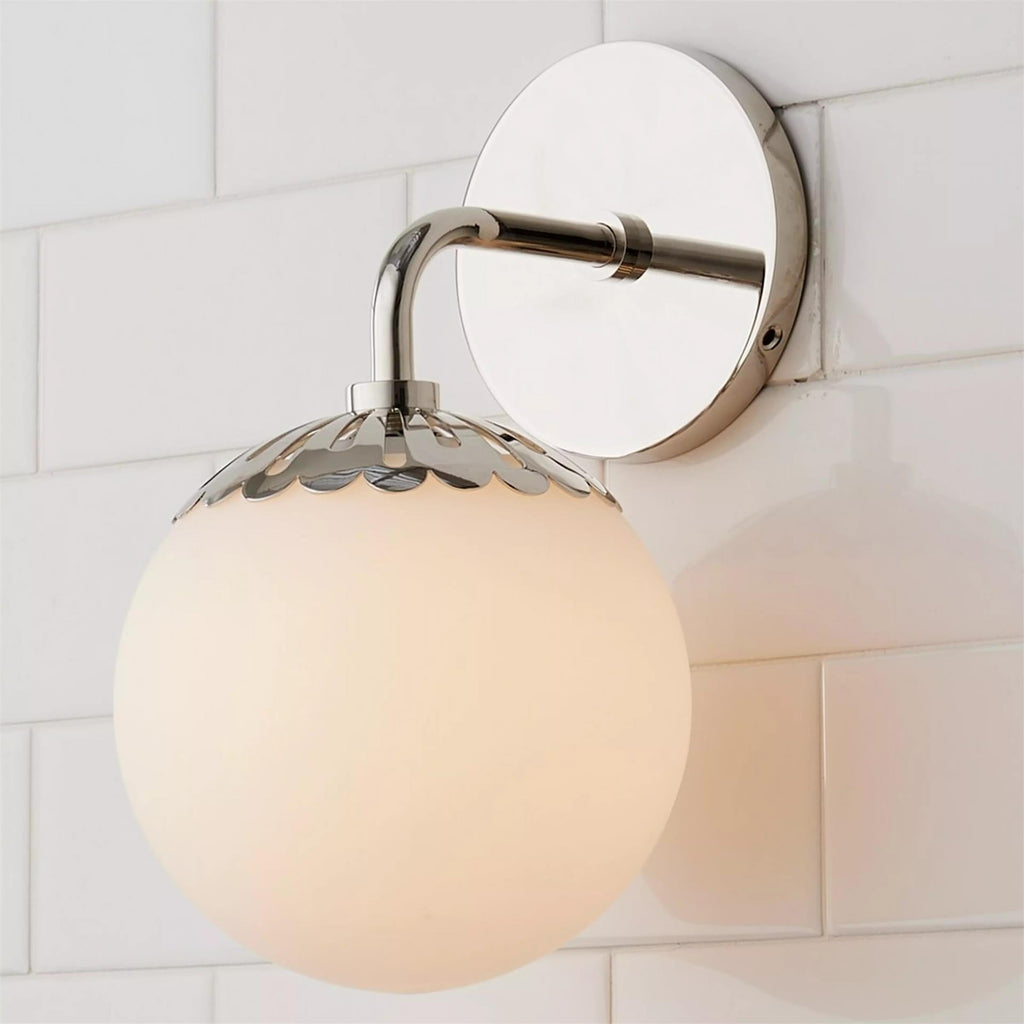 Polished nickel Clérachic Petal-Cap Opal Globe Wall Sconce at an angle, its arm reflecting the white tile.