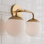 Warm-toned two-head brass Clérachic Petal-Cap Opal Globe Wall Sconce seen at three-quarters on glossy tile.