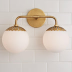 Symmetrical head-on view of the two-head brass Clérachic Petal-Cap Opal Globe Wall Sconce on white tile.