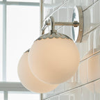 Nickel Clérachic Petal-Cap Opal Globe Wall Sconce with two heads, backlit by a window against glazed tile.