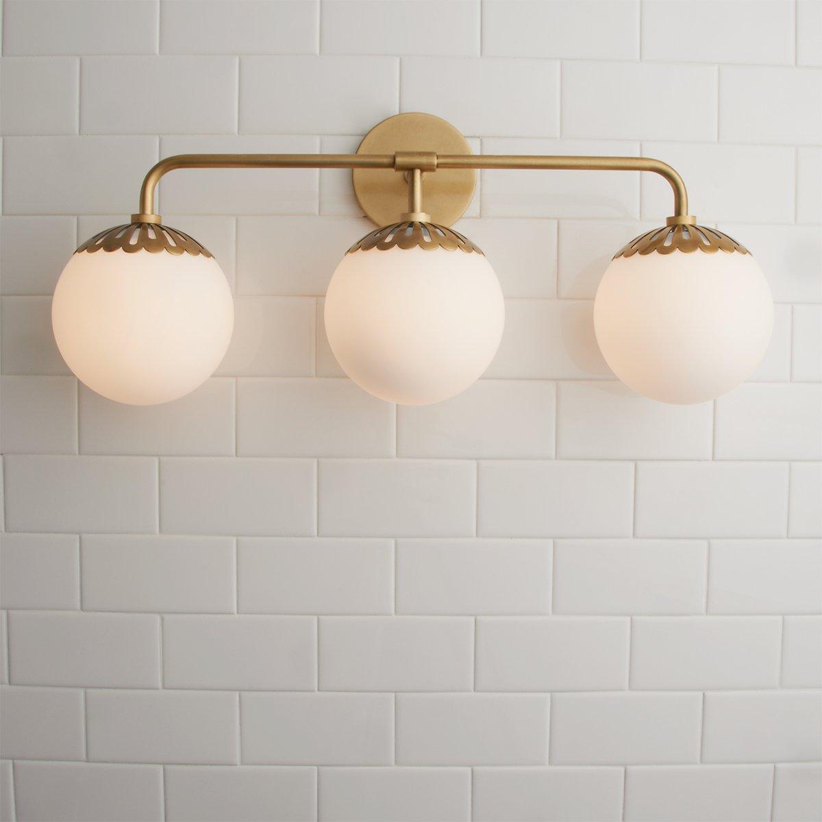 Brass Clérachic Petal-Cap Opal Globe Wall Sconce with three heads, centred head-on above white square tile.