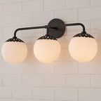 Three-head black Clérachic Petal-Cap Opal Globe Wall Sconce seen slightly from below on white tile.