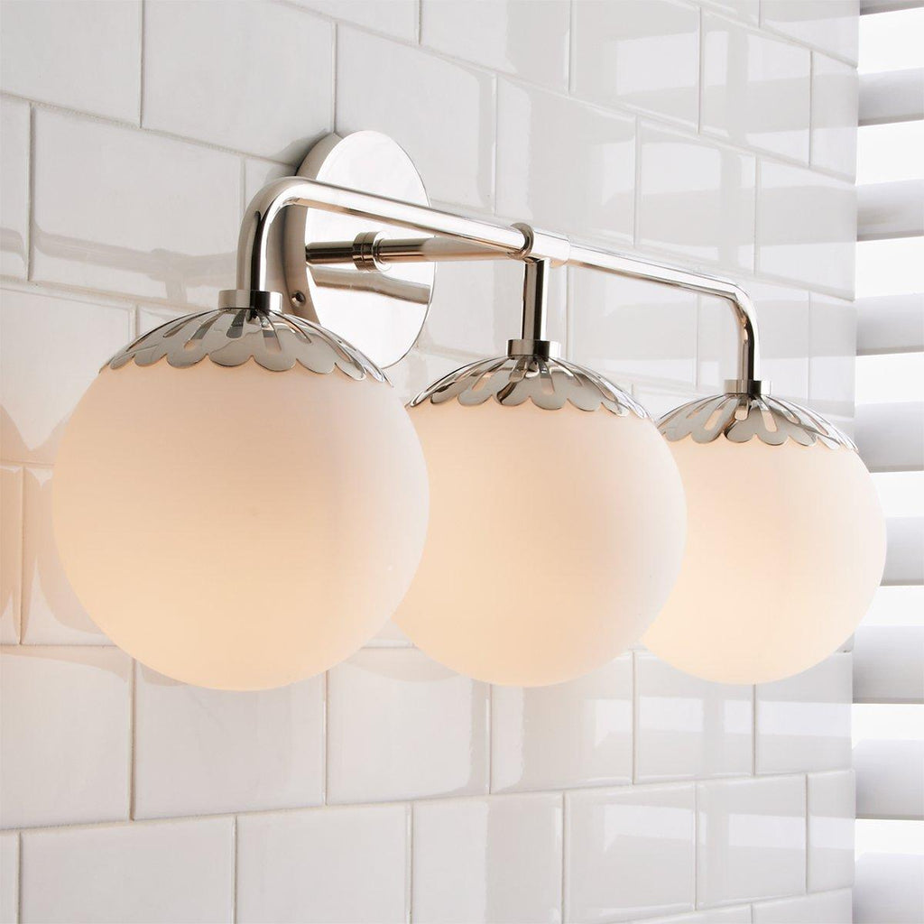Three opal globes of the nickel Clérachic Petal-Cap Wall Sconce lined up in a row beside a bright window.