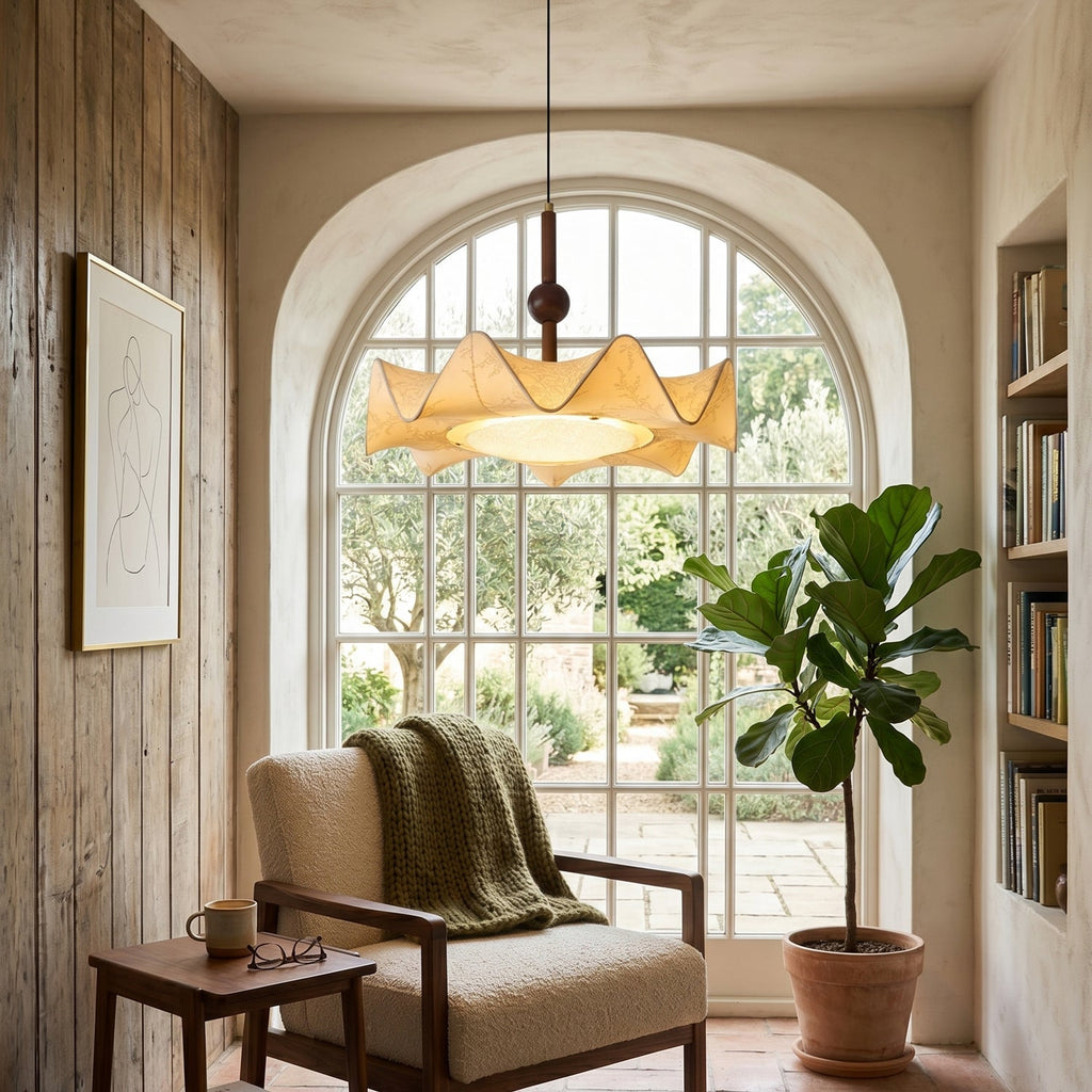 Hanging before a tall arched window, this Clérachic pendant lights a reading corner with a cushioned armchair, a green throw and a potted fiddle-leaf fig.