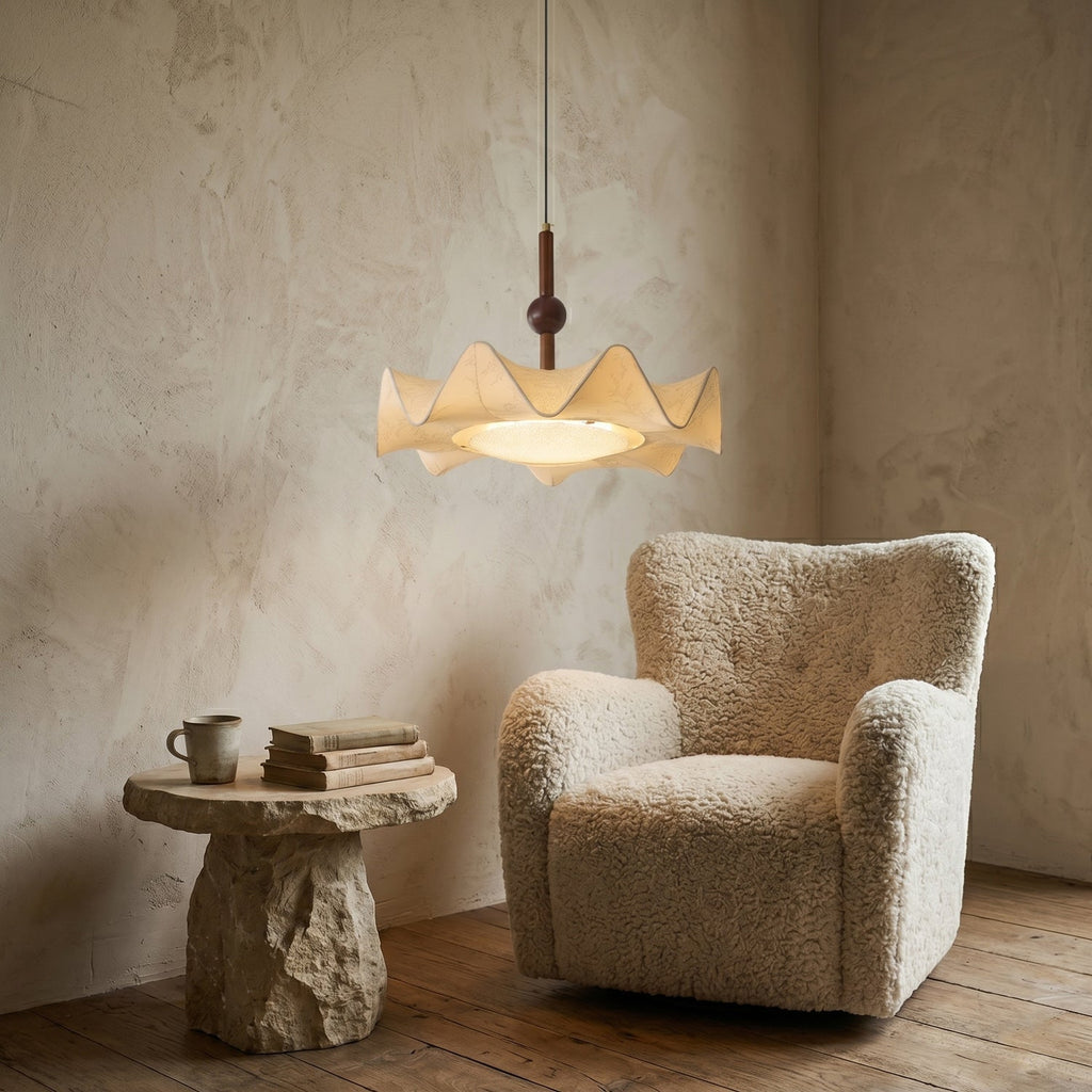 A lit Clérachic pendant on a plaster wall above a boucle armchair and a rough stone side table stacked with books and a mug.
