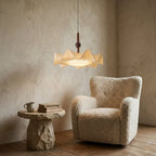 A lit Clérachic pendant on a plaster wall above a boucle armchair and a rough stone side table stacked with books and a mug.