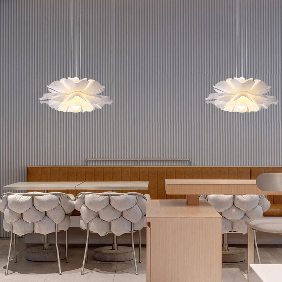 Clérachic petal pendants lit in a pair over a tan leather banquette and scallop-backed chairs in a restaurant.