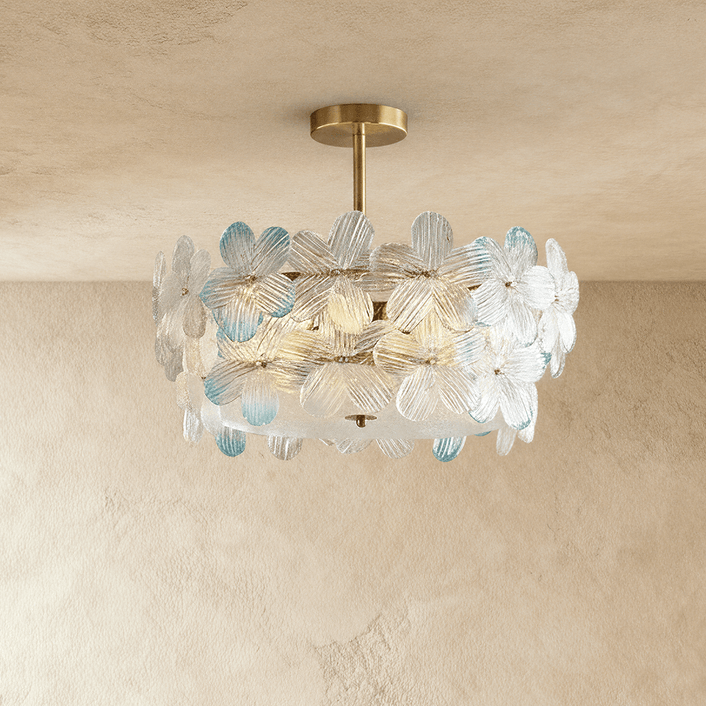 Clérachic brass ceiling light with clear glass petals, a few tipped in pale blue, on a short stem against a limewashed wall.