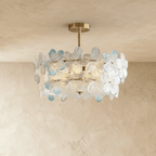 Clérachic brass ceiling light with clear glass petals, a few tipped in pale blue, on a short stem against a limewashed wall.