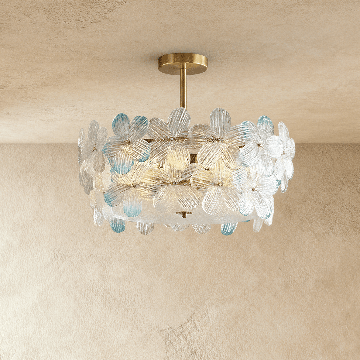Clérachic brass ceiling light with clear glass petals, a few tipped in pale blue, on a short stem against a limewashed wall.