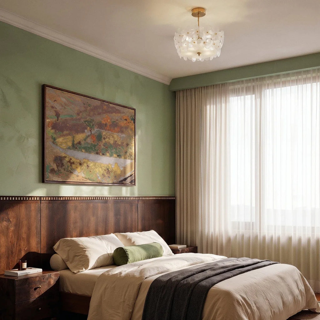 Clérachic glass-flower ceiling light with brass fittings above a bedroom with sage walls, a walnut headboard and sheer curtains.