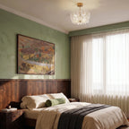 Clérachic glass-flower ceiling light with brass fittings above a bedroom with sage walls, a walnut headboard and sheer curtains.