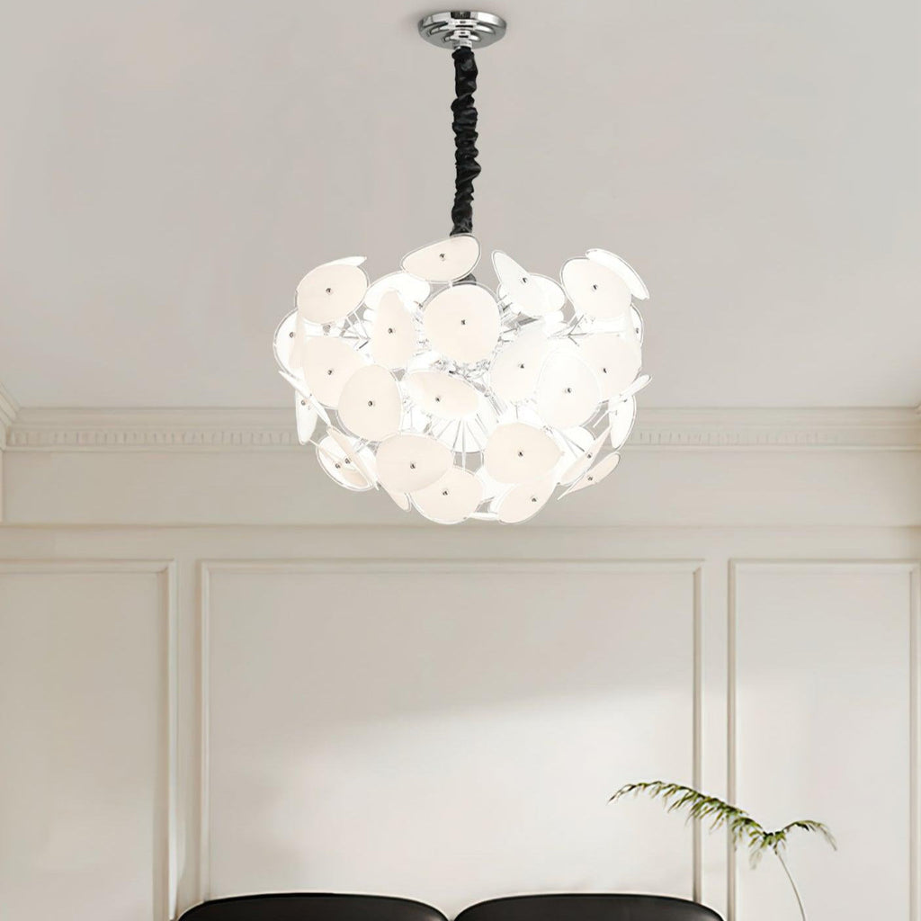 Lit Clérachic Petal Sphere Chandelier beside a window with pleated cellular blinds and a framed chair-design poster.