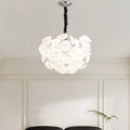 Lit Clérachic Petal Sphere Chandelier beside a window with pleated cellular blinds and a framed chair-design poster.