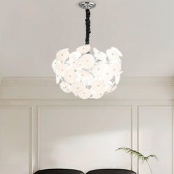 Lit Clérachic Petal Sphere Chandelier beside a window with pleated cellular blinds and a framed chair-design poster.
