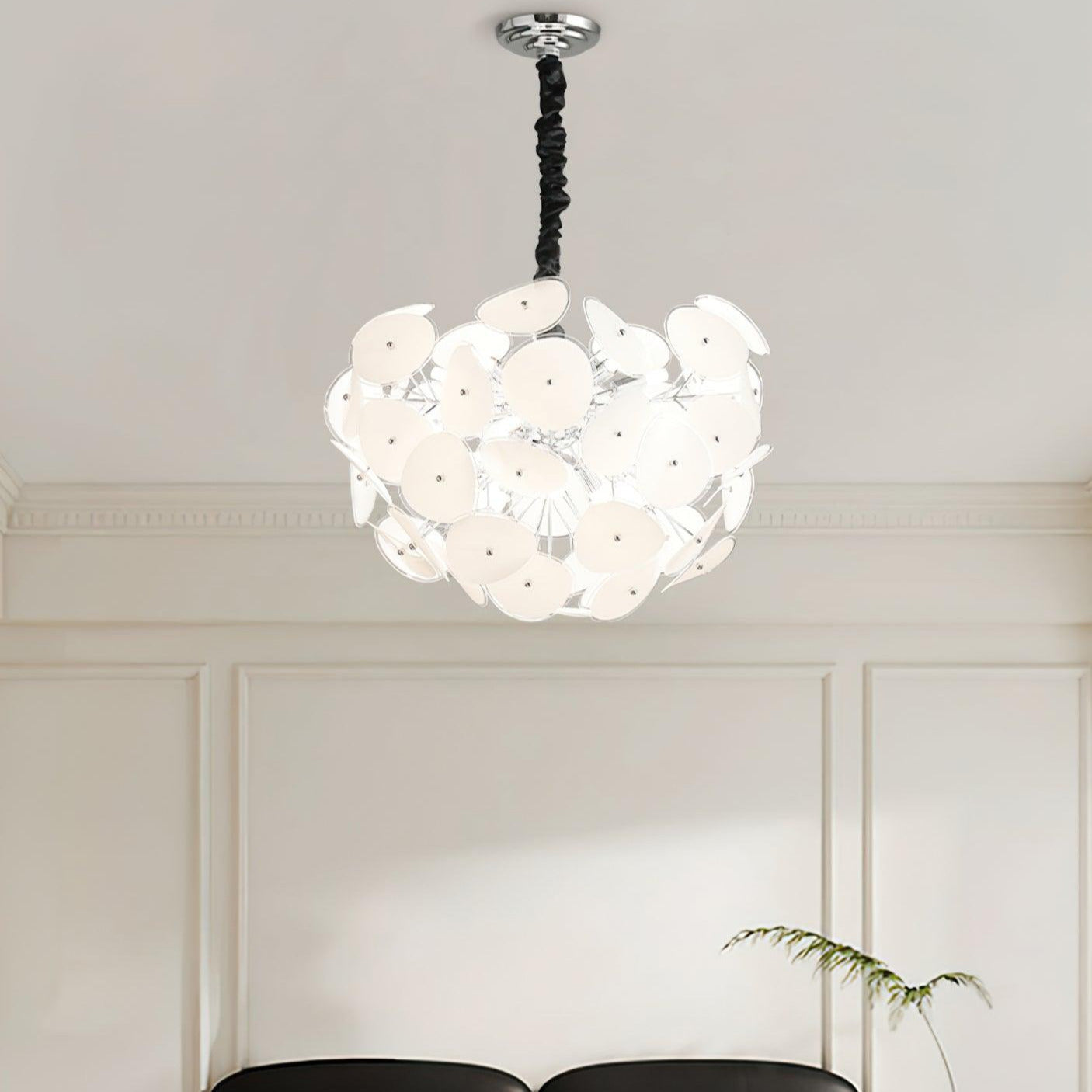 Lit Clérachic Petal Sphere Chandelier beside a window with pleated cellular blinds and a framed chair-design poster.