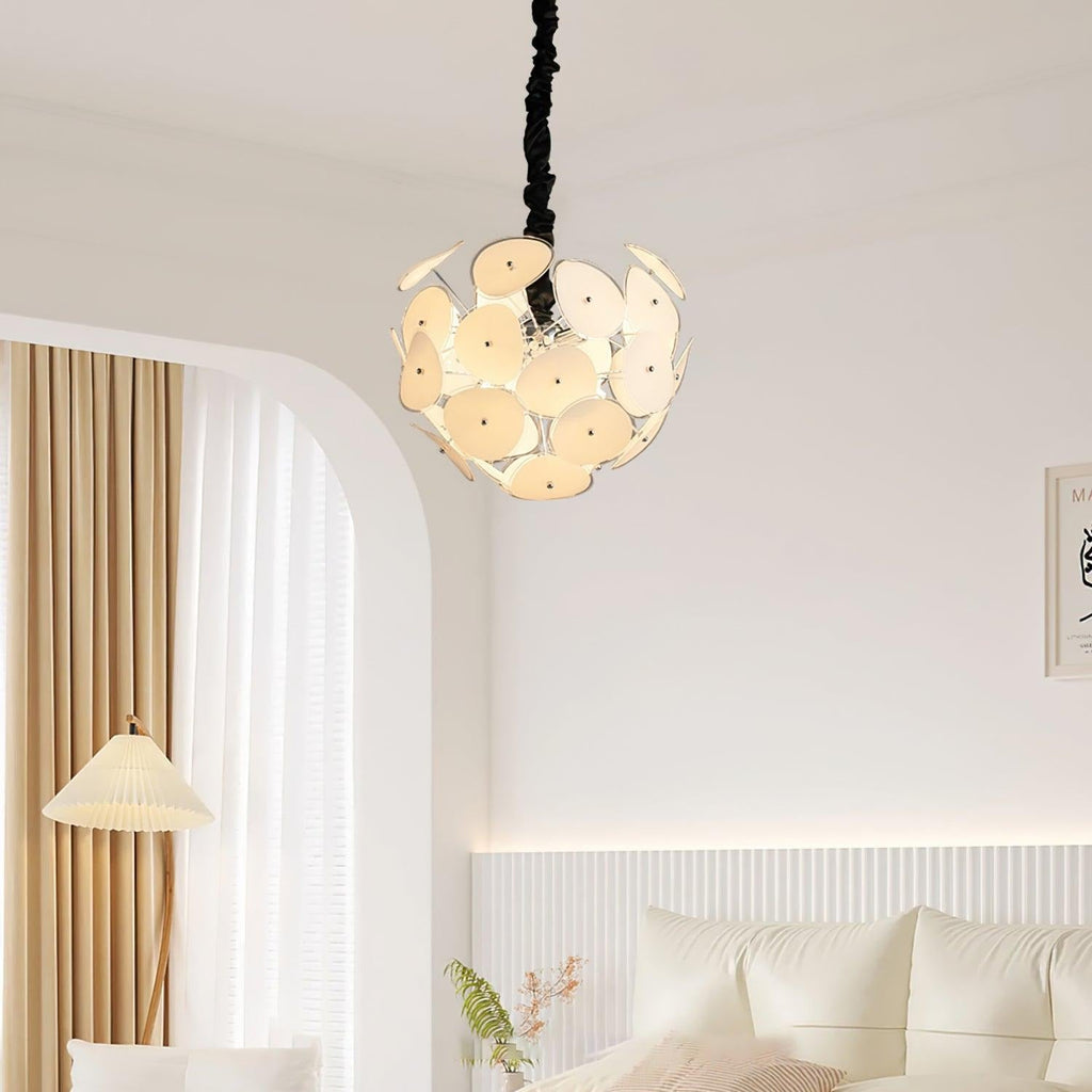 Lit Clérachic Petal Sphere Chandelier above a beige sofa, tall indoor plant and a curved shelving nook.