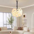 Lit Clérachic Petal Sphere Chandelier over a brown sofa with a cow-print throw, a mounted TV and a city-view window.