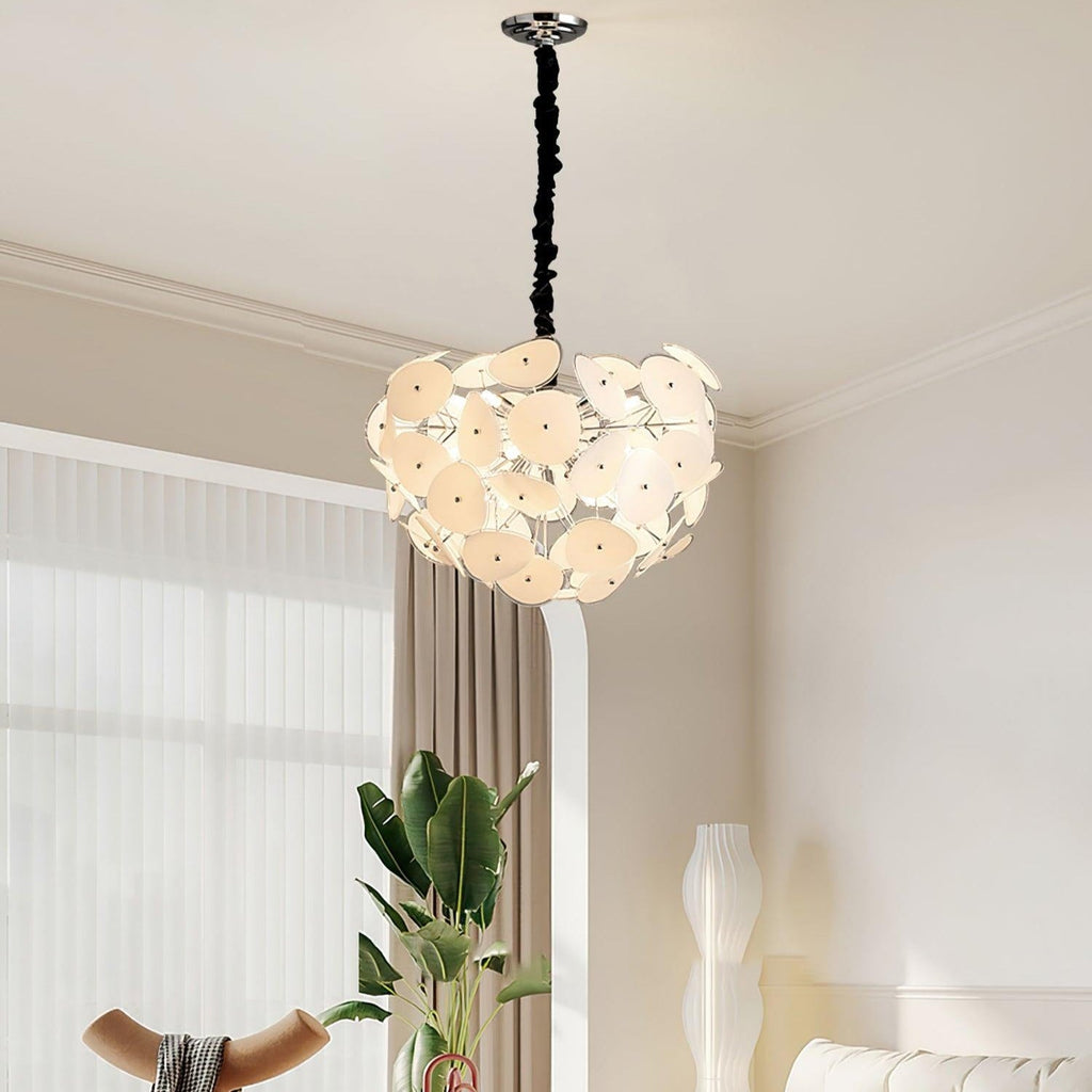 Lit Clérachic Petal Sphere Chandelier in a living room with a green velvet armchair and an artist's easel.