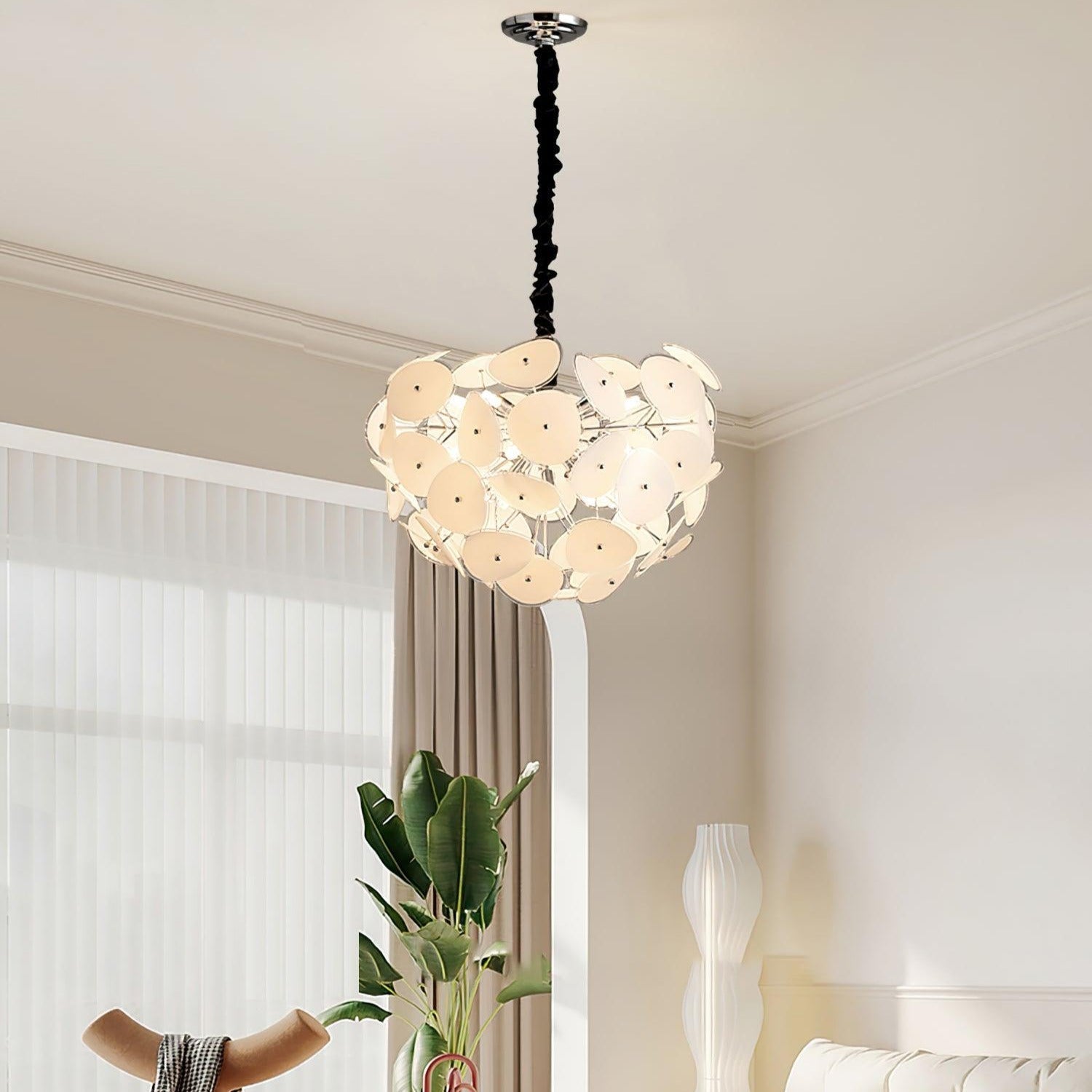 Lit Clérachic Petal Sphere Chandelier in a living room with a green velvet armchair and an artist's easel.