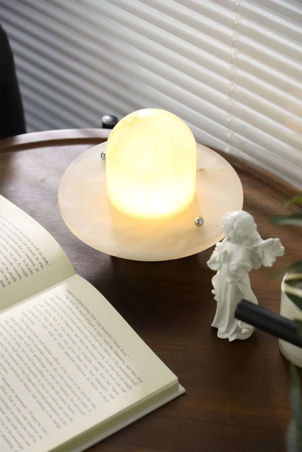 Clérachic Petrified table lamp glowing on a round wooden table, daylight diffused by blinds.