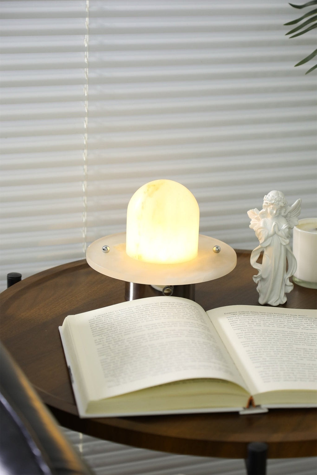 The Clérachic Petrified lamp on a side table with a book and a small figurine at dusk.