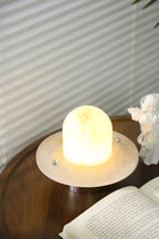 Clérachic Petrified lamp glowing on a book-strewn table in front of pleated blinds.