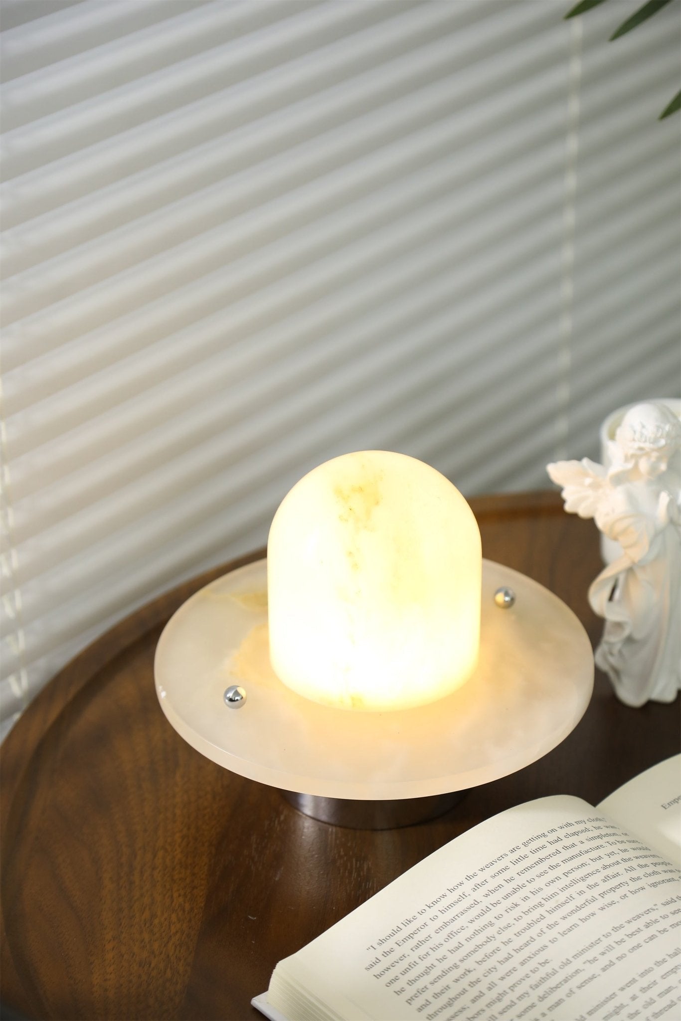 Clérachic Petrified lamp glowing on a book-strewn table in front of pleated blinds.